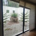 Indoor view looking out to a small, private courtyard with unkempt grass, a modern round planter, and a glimpse of the sky through a window